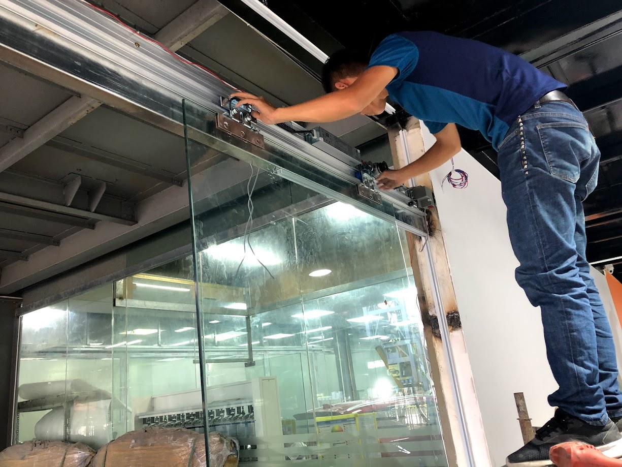 Mô tơ và ray trượt cửa cuốn tự động gắn trên trần nhà xưởng, phía dưới là khu vực đỗ xe ô tô